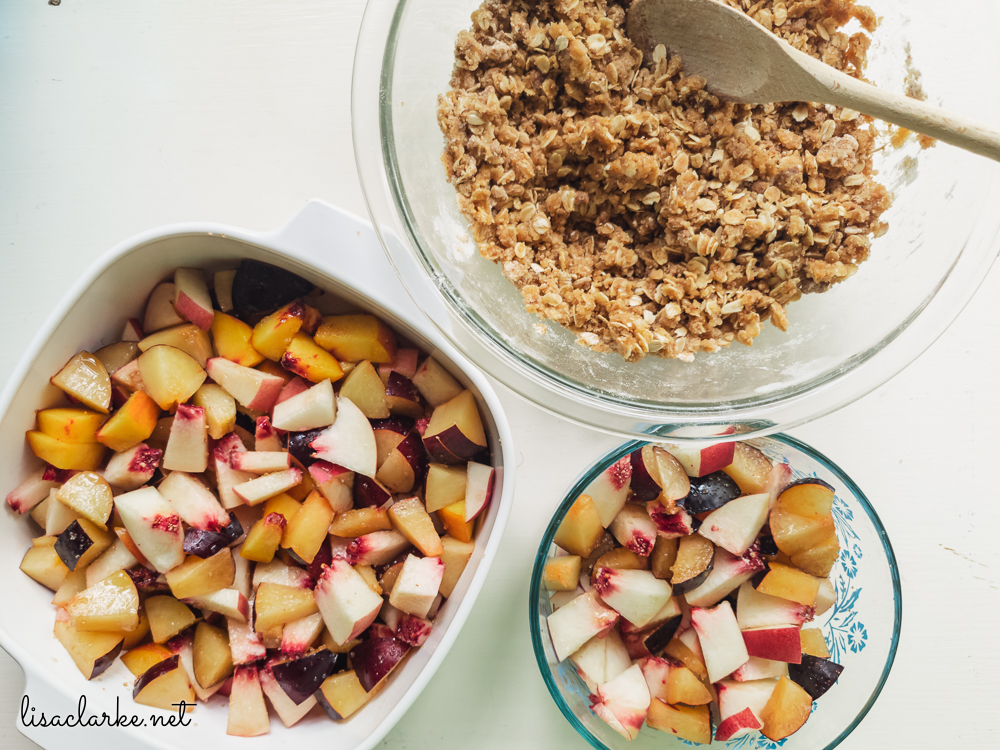 Peaches, plums, and sugar in two bowls, crisp topping in another bowl, for Ginger Peach and Plum Crisp